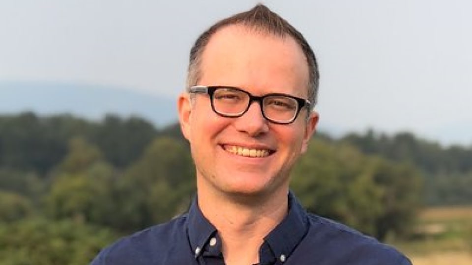 Jeremy Crawford in profile wearing a pair of glasses and a blue shirt standing on top of a hill.