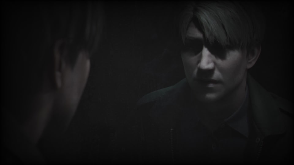 A screenshot from the Silent Hill 2 remake, it shows James Sunderland looking into a dirty dark mirror, his eyes covered in shadow.