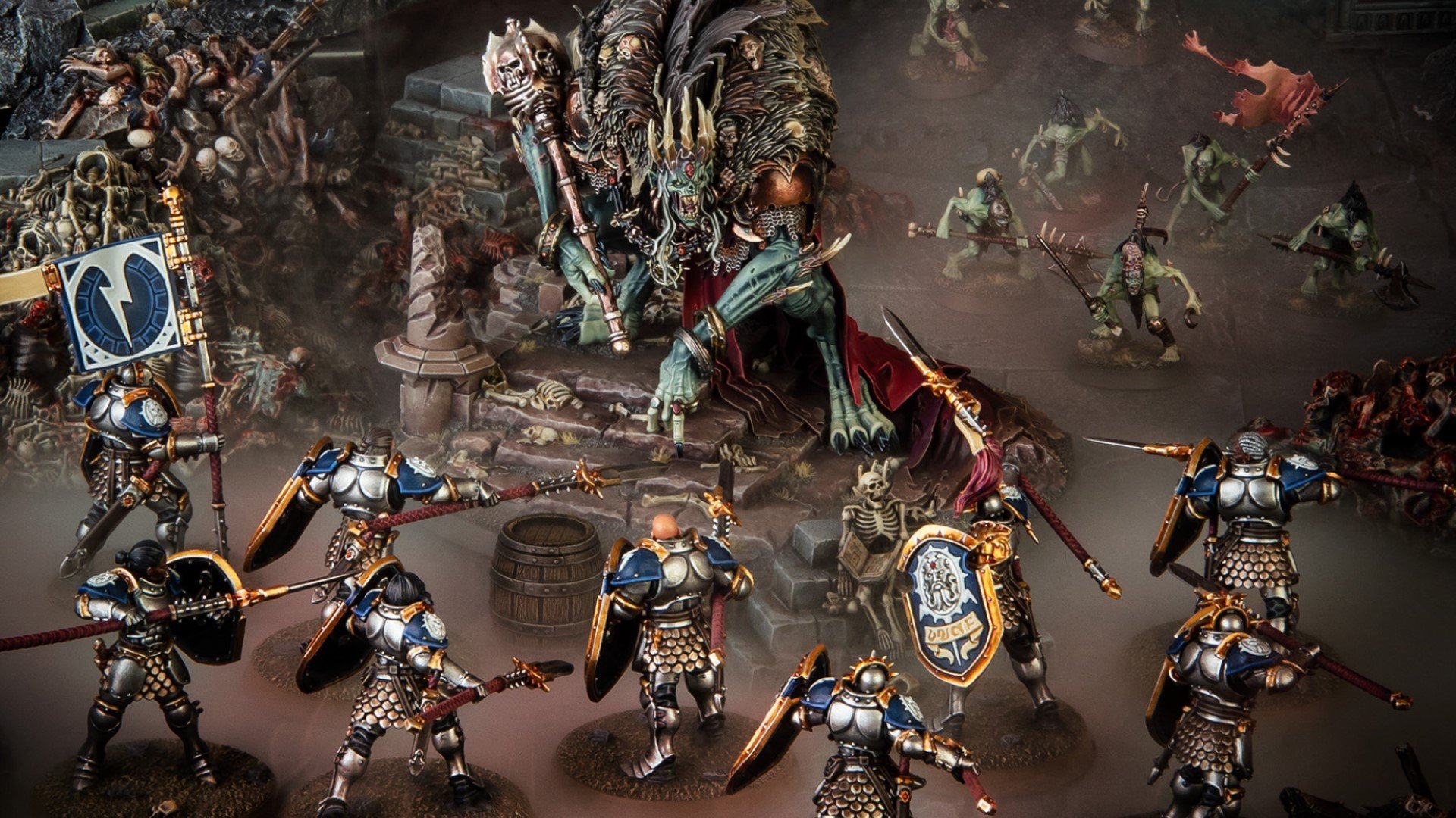 A collection of miniatures, one of a giant undead wearing a crown surrounded by knights in armor, on a blasted battlefield.