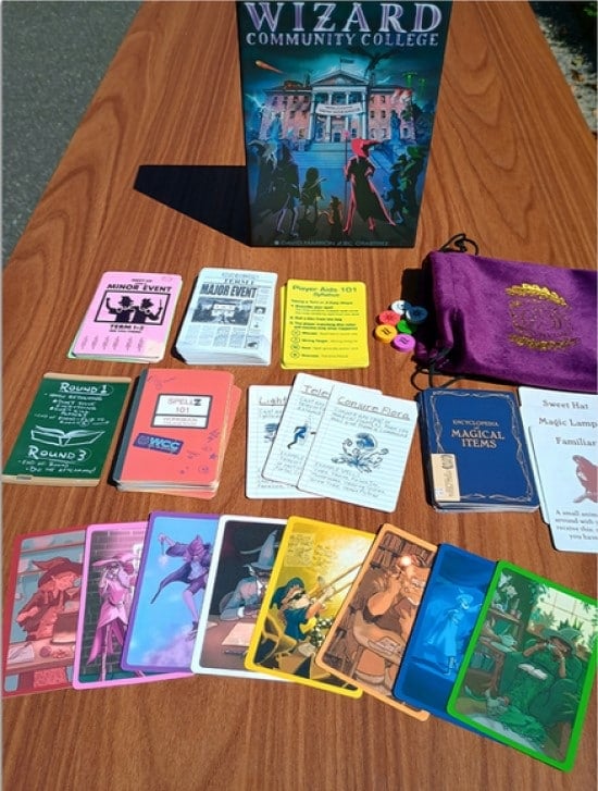 A spread of cards, a drawstring bag, and the Wizard Community College game box, all on a wooden desk.